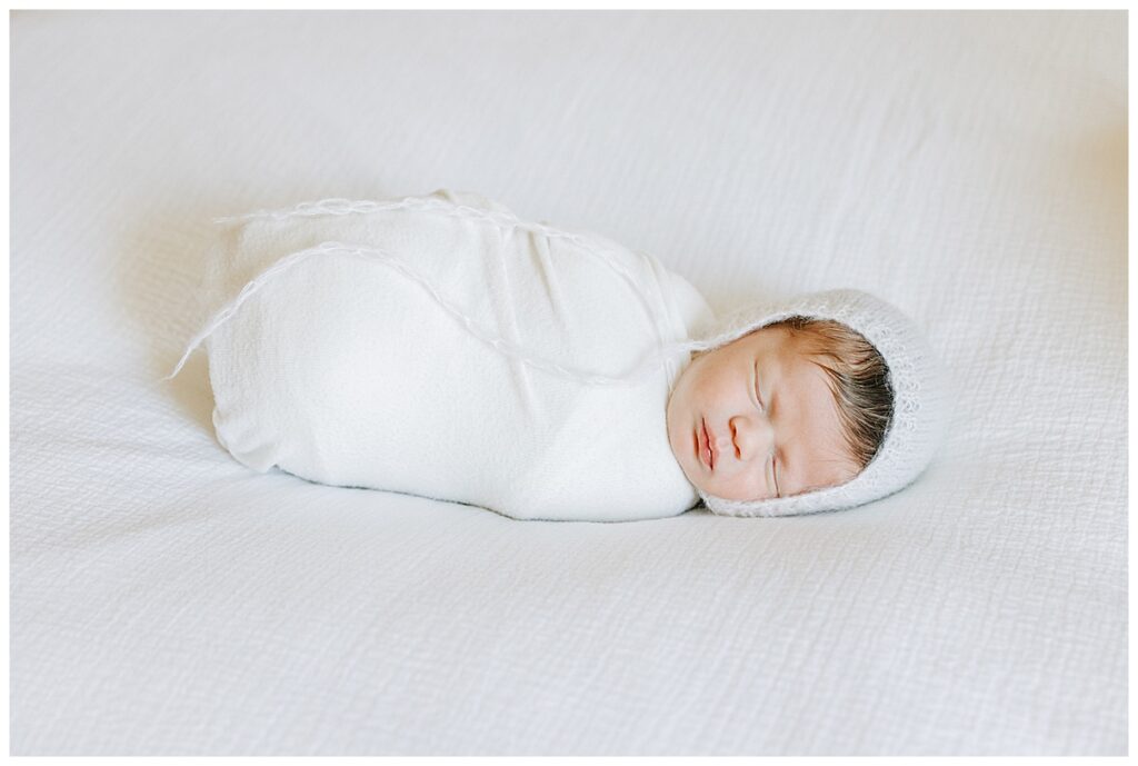 newborn girl swaddles in white with a bonnet 