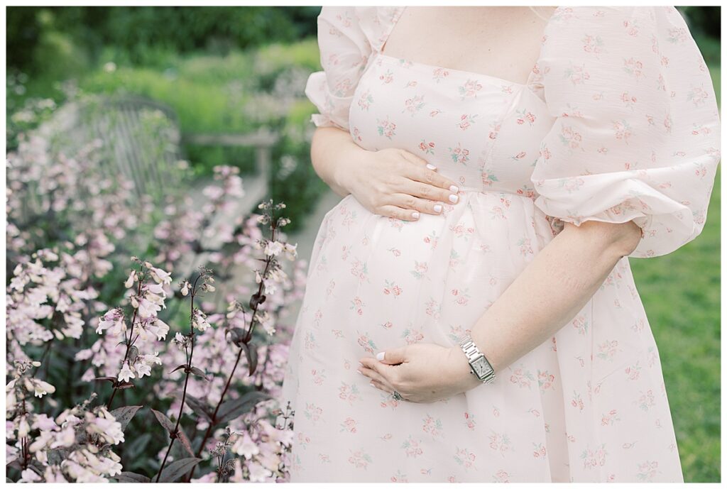 mother holding her baby bump next to purple flowers 