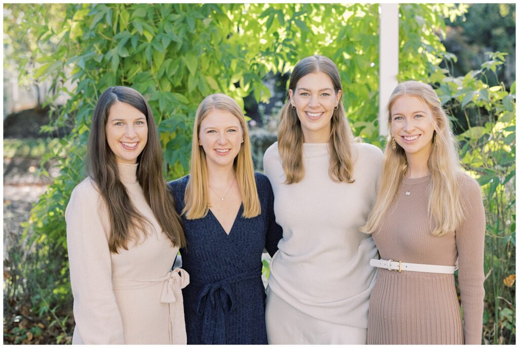 four sisters smiling and standing tougher with lush green background 